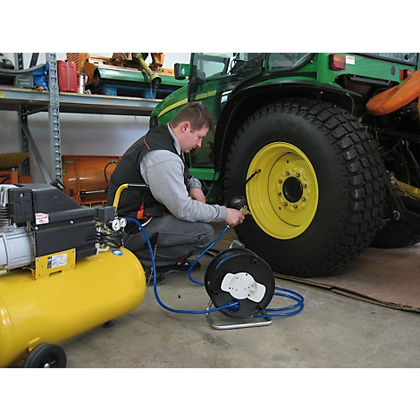 Man inflating tractor tire with compressed air. Yellow compressor and green tractor in the background.