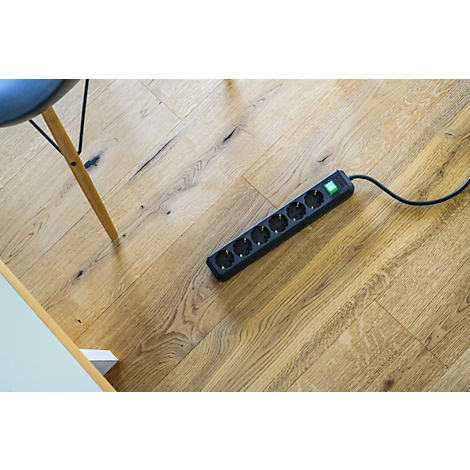 Multiprise noire sur parquet. Une chaise et une table sont coupées.