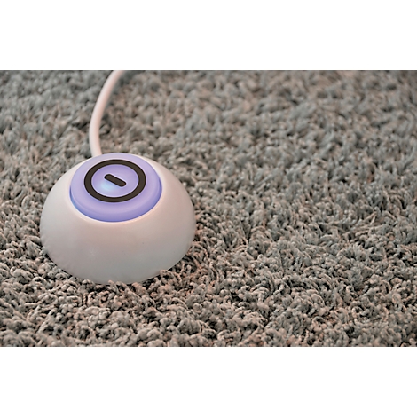 Appareil rond blanc avec lumière bleue et symbole noir sur tapis gris.