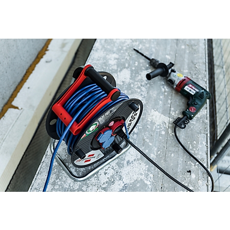 Dévidoir avec câble bleu et poignée rouge, à côté d'une perceuse sur un sol en béton.