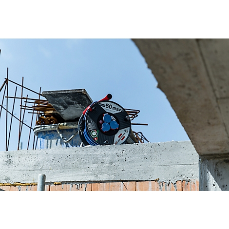 Enrouleur de câble avec prises sur un chantier de construction. Armature en acier et ciel bleu en arrière-plan.