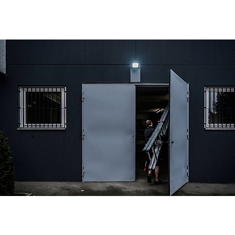 Eine Person installiert einen schwarzen LED-Strahler an einer Wand.