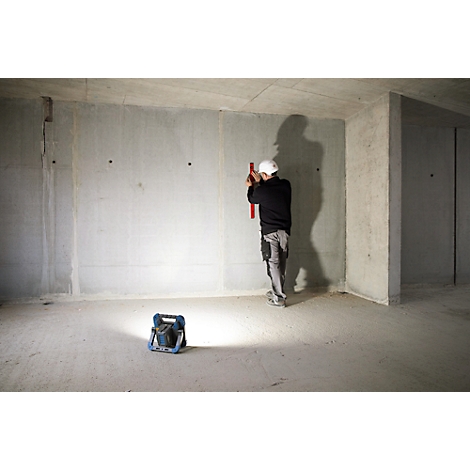 Un ouvrier du bâtiment mesure le mur avec un niveau à bulle dans une construction brute. Au premier plan, une lampe de chantier.