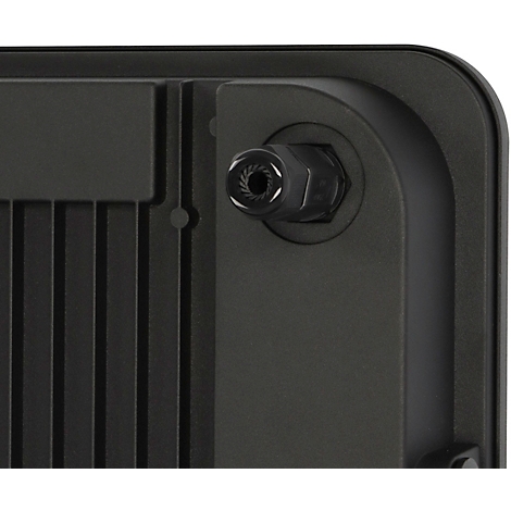 Un éclairage LED extérieur sur un mur de maison sombre. A côté, des plantes vertes.