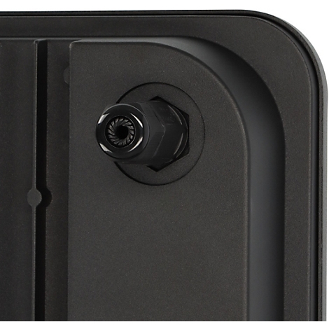 Un projecteur LED éclaire une clôture. Environnement sombre avec des feuilles vertes.