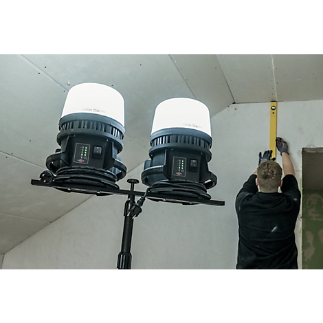 Twee bouwlampen verlichten een bouwplaats. Een arbeider richt een muur uit met een waterpas.