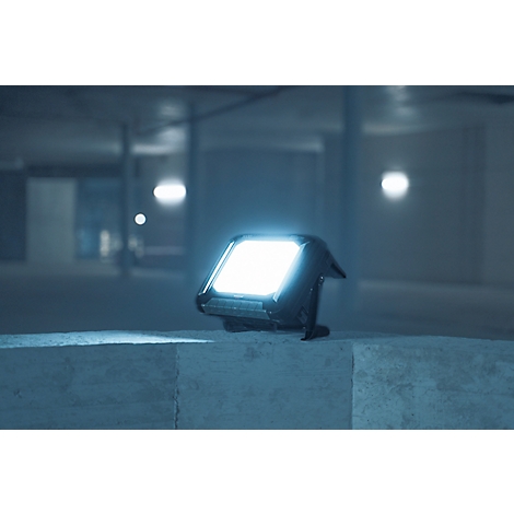 Lampe LED lumineuse posée sur une surface en béton, avec un parking souterrain en arrière-plan. La lumière brille dans un environnement sombre.