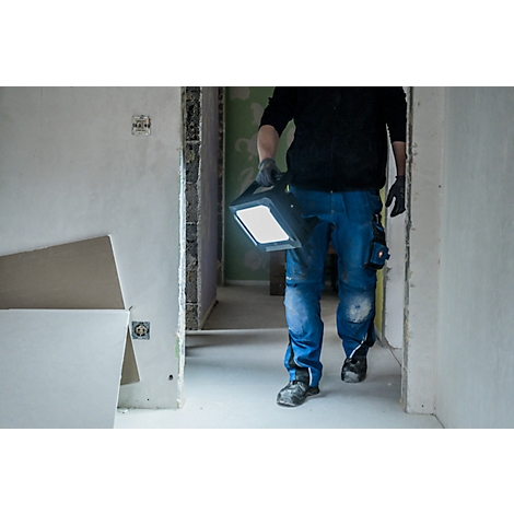 Persoon met handschoenen en heldere werklamp in onafgewerkte kamer. Blauwe broek, zwart topje.