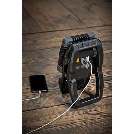 Zwarte werklamp met geïntegreerde powerbank laadt een smartphone op. Op houten ondergrond.