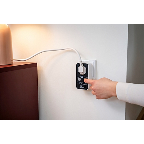 Une main actionnant une minuterie branchée sur une prise murale.