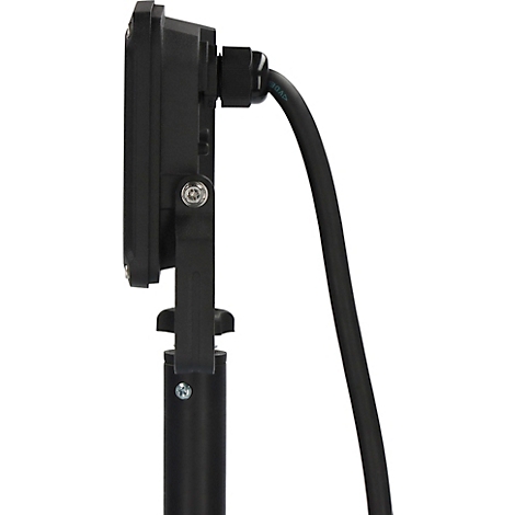 Pièce sombre avec mur humide. Projecteur sur trépied, flaque d'eau au sol.