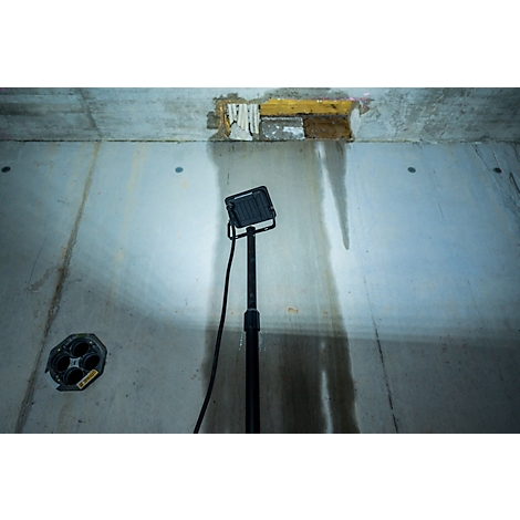 Ein Arbeitslicht beleuchtet eine Betonwand, an der Wasser entlangläuft. Oben befindet sich ein beschädigter Bereich.