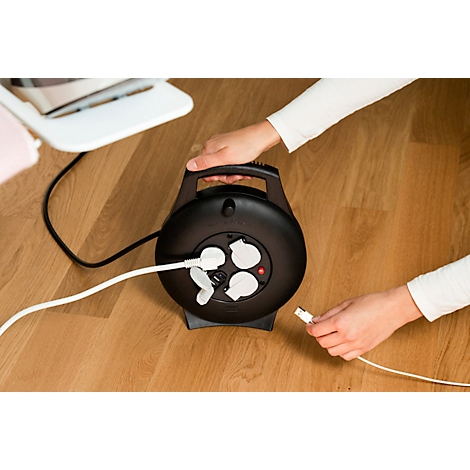 Nahaufnahme einer schwarzen runden Steckdosenleiste mit weißen Steckdosenabdeckungen und einer roten LED. Ein weißes Kabel ist eingesteckt.