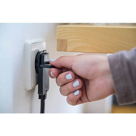 Eine Hand steckt einen schwarzen Stecker in eine weiße Steckdose.