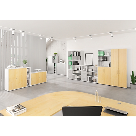 Een modern kantoor met licht houten meubilair. Diverse kasten en planken, sommige gevuld met groene mappen, bepalen het beeld. Een bureau en planten maken het plaatje compleet.