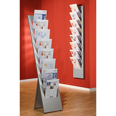Two silver brochure stands with brochures in front of a red wall. The right stand is mounted on the wall.