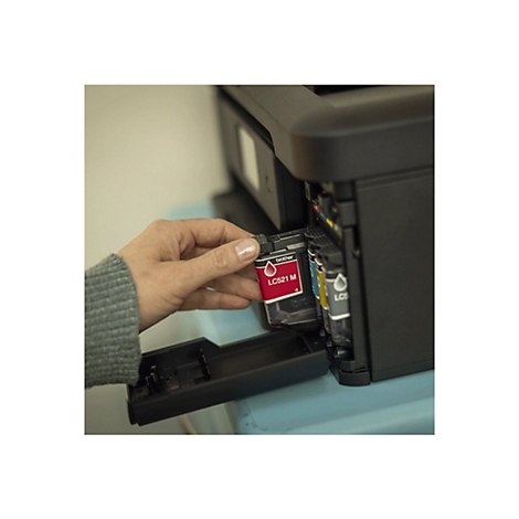 Eine Hand setzt eine rote Tintenpatrone in einen Drucker ein. Auf der Patrone steht LC521 M.