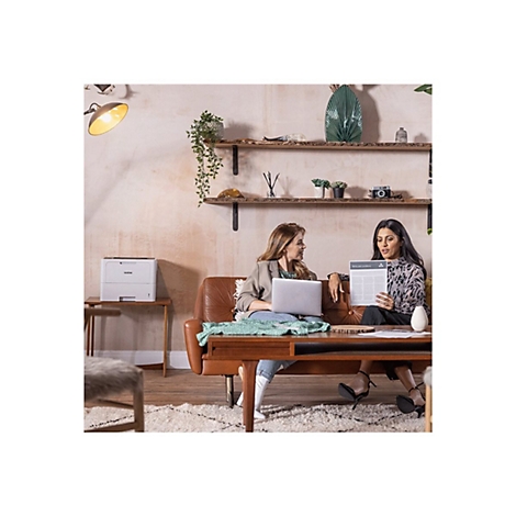 Zwei Frauen sitzen auf einem Sofa. Eine hält ein Dokument, die andere einen Laptop.