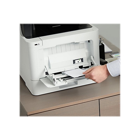 Eine Person legt Papier in einen weiÃŸen Drucker ein. Der Drucker steht auf einem Schreibtisch aus Holz.