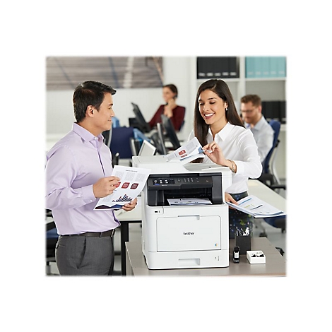 Zwei Personen schauen auf Ausdrucke, die aus einem weiÃŸen Brother-Multifunktionsdrucker kommen. Im Hintergrund weitere Personen im BÃ¼ro.