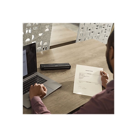 Person am Tisch mit Laptop und Drucker. Er hält einen Vertrag in der Hand.