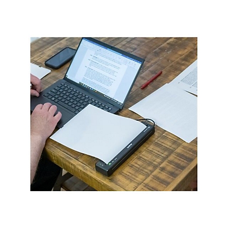 Person arbeitet an einem Laptop. Ein Blatt Papier liegt in einem Scanner. Auf dem Holztisch sind auch Smartphone und Stift.
