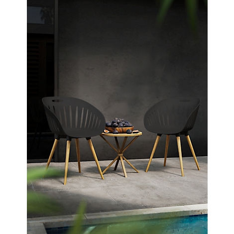 Twee zwarte stoelen met houten poten en een kleine tafel met fruit staan voor een donkere muur.
