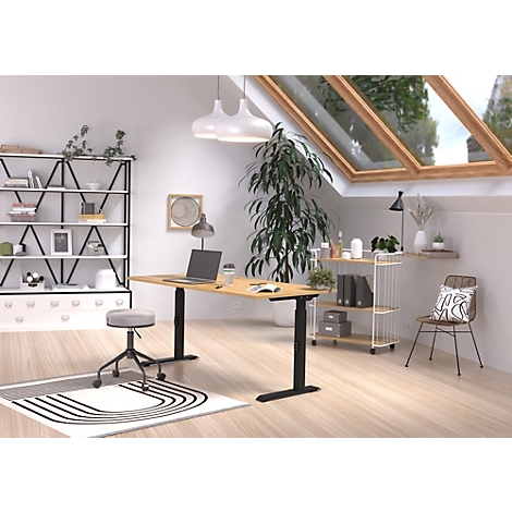 Un bureau à domicile lumineux avec un bureau réglable en hauteur, un ordinateur portable, des étagères et une chaise. Une fenêtre offre une vue sur l'extérieur.