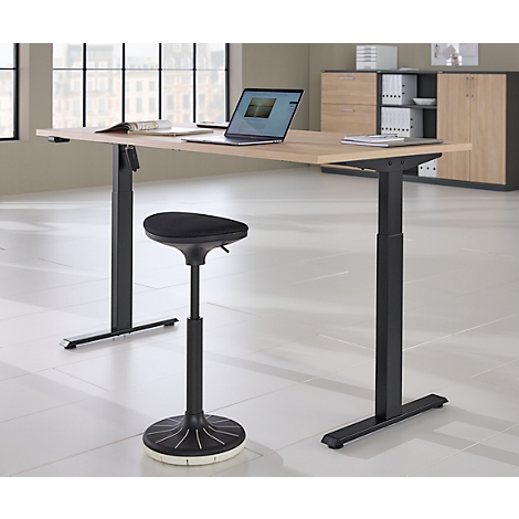 Een in hoogte verstelbaar bureau met een laptop en kruk in een modern kantoor. Een kast en een raam op de achtergrond.