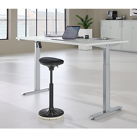 In hoogte verstelbaar bureau met laptop en kruk. Ramen en kasten op de achtergrond.