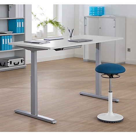 Un bureau réglable en hauteur avec une chaise dans un bureau moderne. Des ordinateurs portables et des fournitures de bureau sont sur la table.