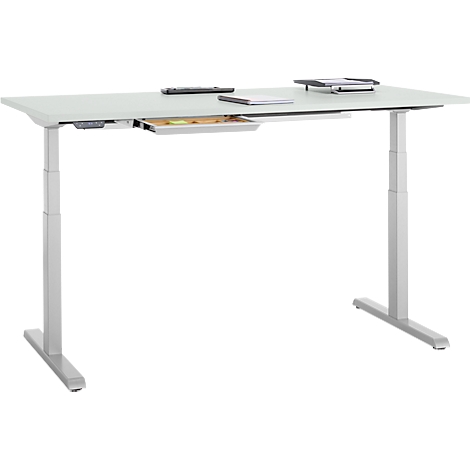 Bureau gris réglable en hauteur avec tiroir et articles. Ordinateur portable, tablette et télécommande sont dessus.