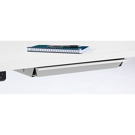 Gros plan sur un bureau avec un passe-câbles argenté sous le plateau. Un bloc-notes avec un stylo repose sur le dessus.