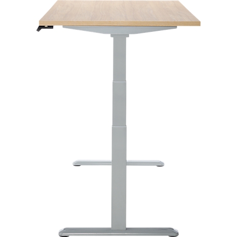 Un bureau réglable en hauteur avec un plateau de table brun clair et un cadre gris. Le plateau de table est rectangulaire, le cadre se compose d'un pilier et d'un pied.