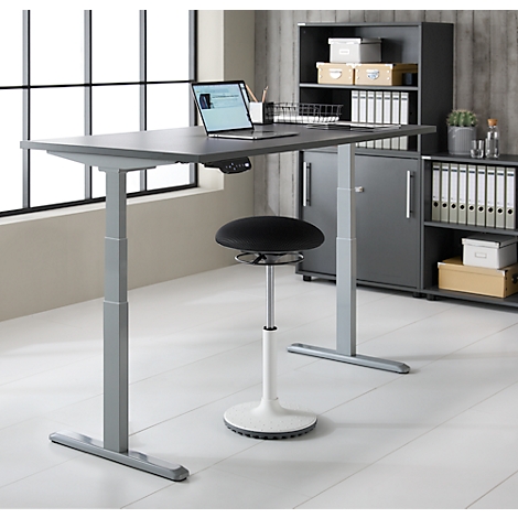 Bureau debout gris avec ordinateur portable, tabouret noir et armoire grise. L'arrière-plan est une fenêtre et un mur en bois.