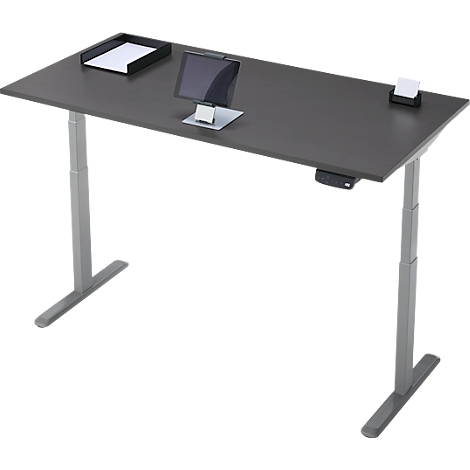 Bureau réglable en hauteur, gris foncé, avec tablette, porte-papier et bloc-notes. Le bureau repose sur deux pieds gris.