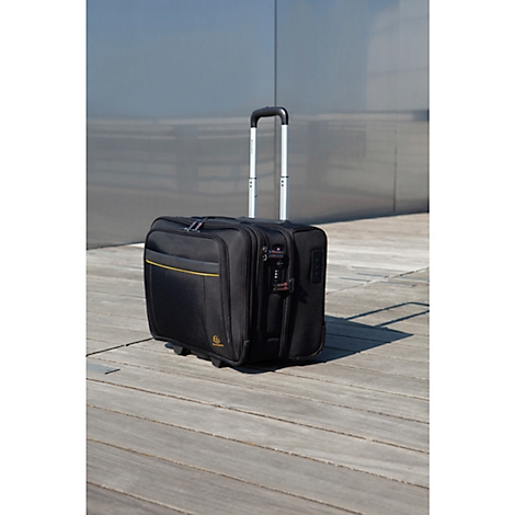Black rolling suitcase with extendable handle standing on wooden planks against a gray background.