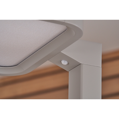 Close-up of a corner with a sensor. An angular pillar meets a rounded corner. In the corner is a small, round sensor. A shaded fabric is to the left.