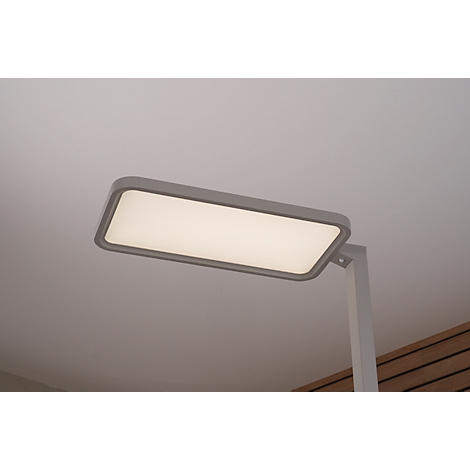 Rectangular, grey LED desk lamp, illuminated. Bright background.