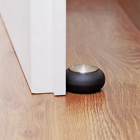 Un butoir de porte en caoutchouc noir maintenant une porte blanche ouverte sur un plancher en bois.