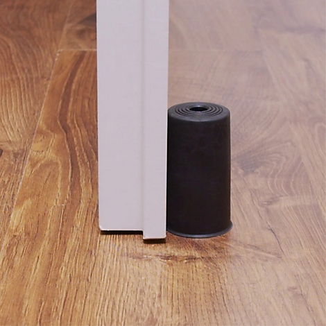 Butoir de porte noir au sol. Il empêche la porte de se fermer. Plancher en bois.