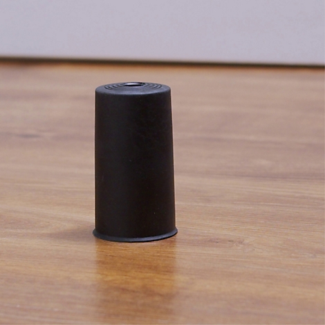 Un patin de meuble noir et cylindrique se dresse sur un sol en bois, qui a une ligne noire d'un côté.