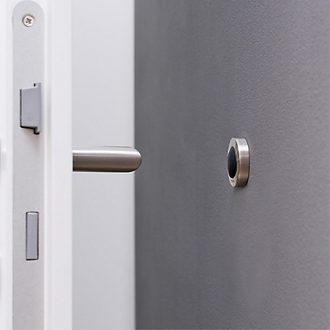 Gros plan d'une porte blanche avec poignée en acier inoxydable et d'un ouvre-porte avec intérieur sombre sur un mur gris.