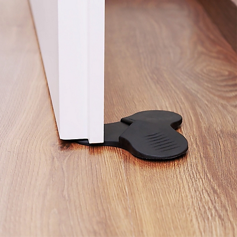 Butée de porte en caoutchouc noir sous une porte blanche sur un plancher en bois.