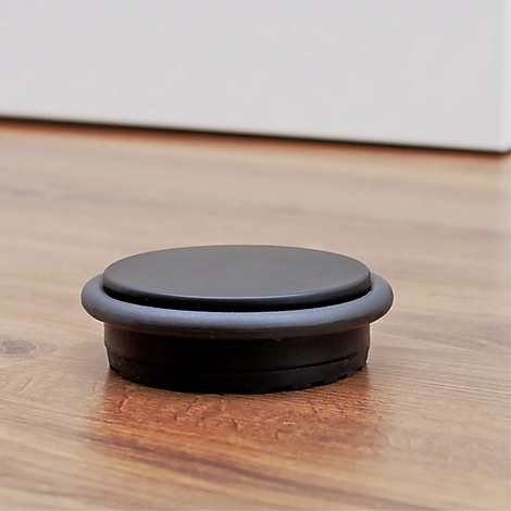 Un butoir de porte noir sur un plancher en bois. Le butoir a une forme ronde et un anneau en caoutchouc.