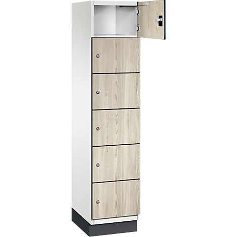 Hoge locker met 6 compartimenten, waarvan één open. De deuren hebben een lichte houtlook, de body is wit.