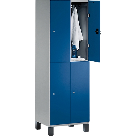 Ein blauer Spind mit geöffneter Tür. Im Inneren hängen ein weißes Hemd und Kosmetikartikel auf einem Regal.