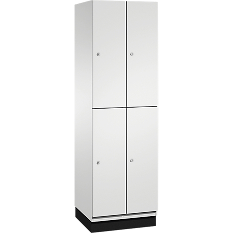 Ein weißer Schrank mit vier Türen und kleinen runden Knöpfen. Der Schrank steht auf einem schwarzen Sockel.