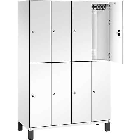 Weißer Spind mit 8 Fächern. Eine Tür ist geöffnet, dahinter Haken und ein kleines Lochgitter.
