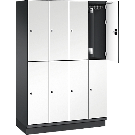 Acht Spinde, weiß mit schwarzen Rahmen. Eine Tür ist geöffnet und zeigt das Innere mit Kleiderhaken.